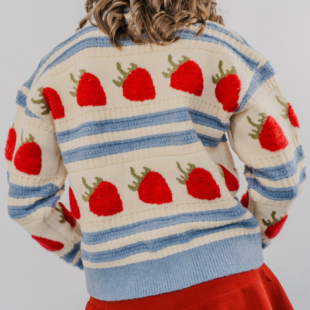 Back view of the model wearing "The Perfect Pick Cardigan". The sweater is blue and beige striped with strawberries covering it in a line.