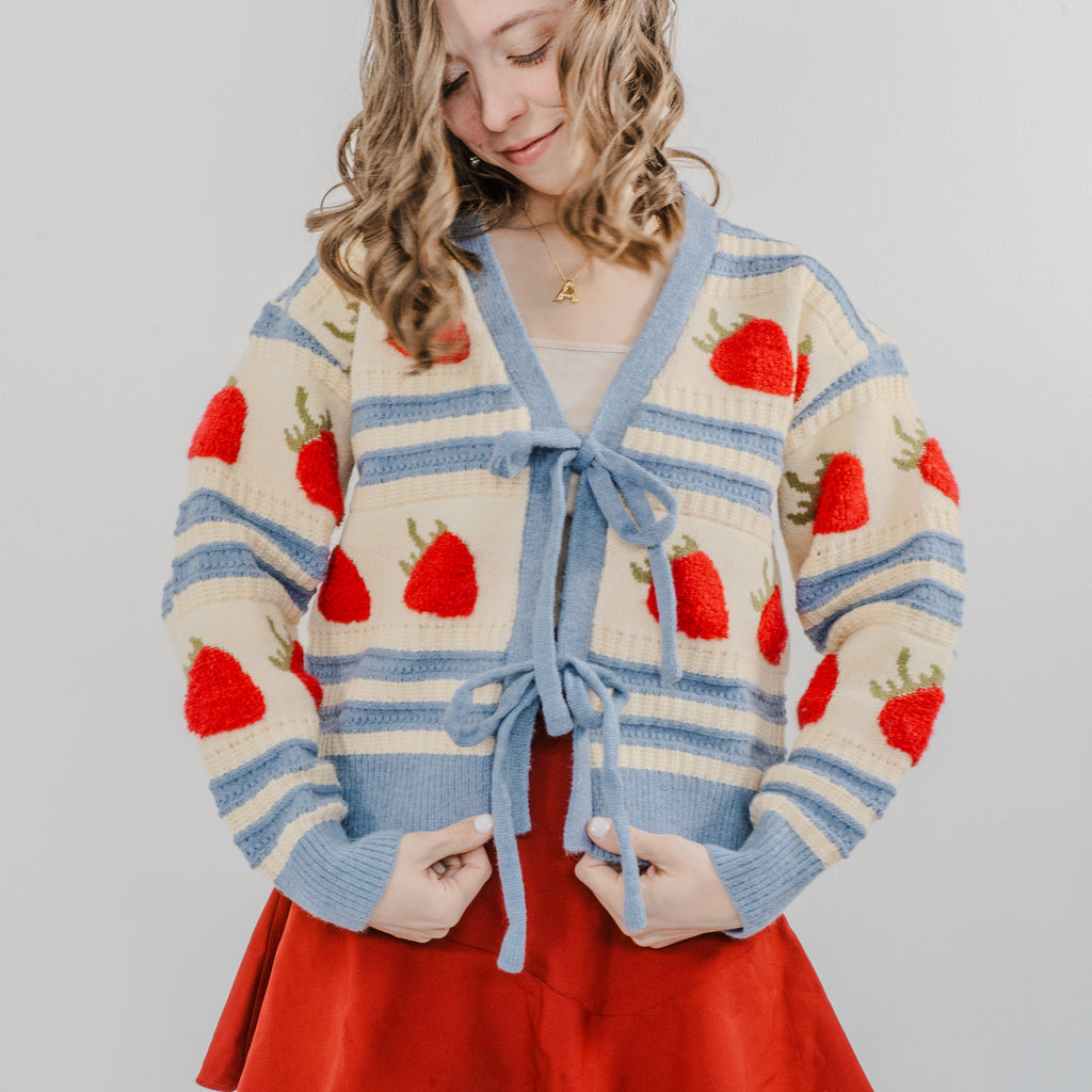 Model wearing "The Perfect Pick Cardigan" and showing the details close up. Paired with a red skirt.