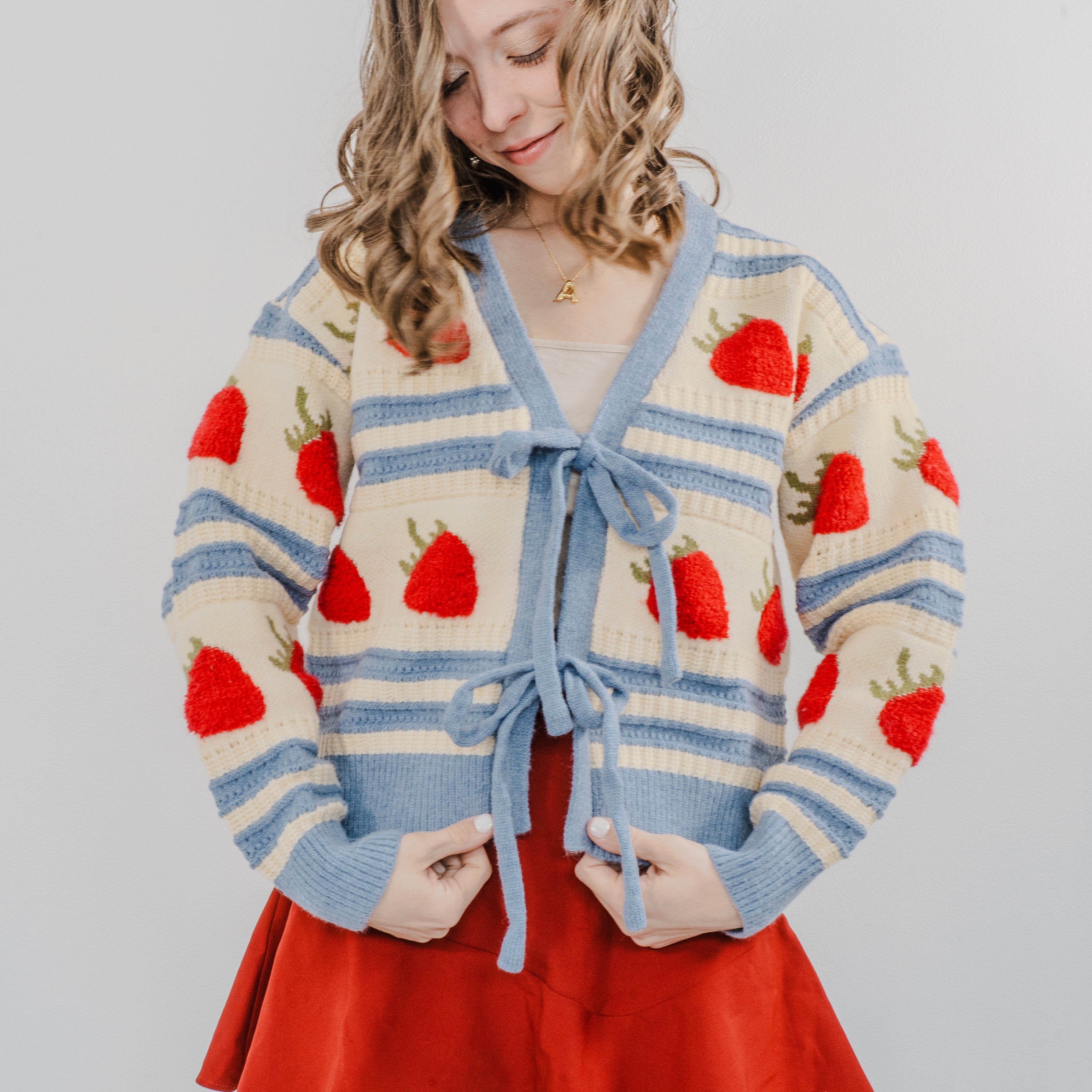 Model wearing "The Perfect Pick Cardigan" and showing the details close up. Paired with a red skirt.