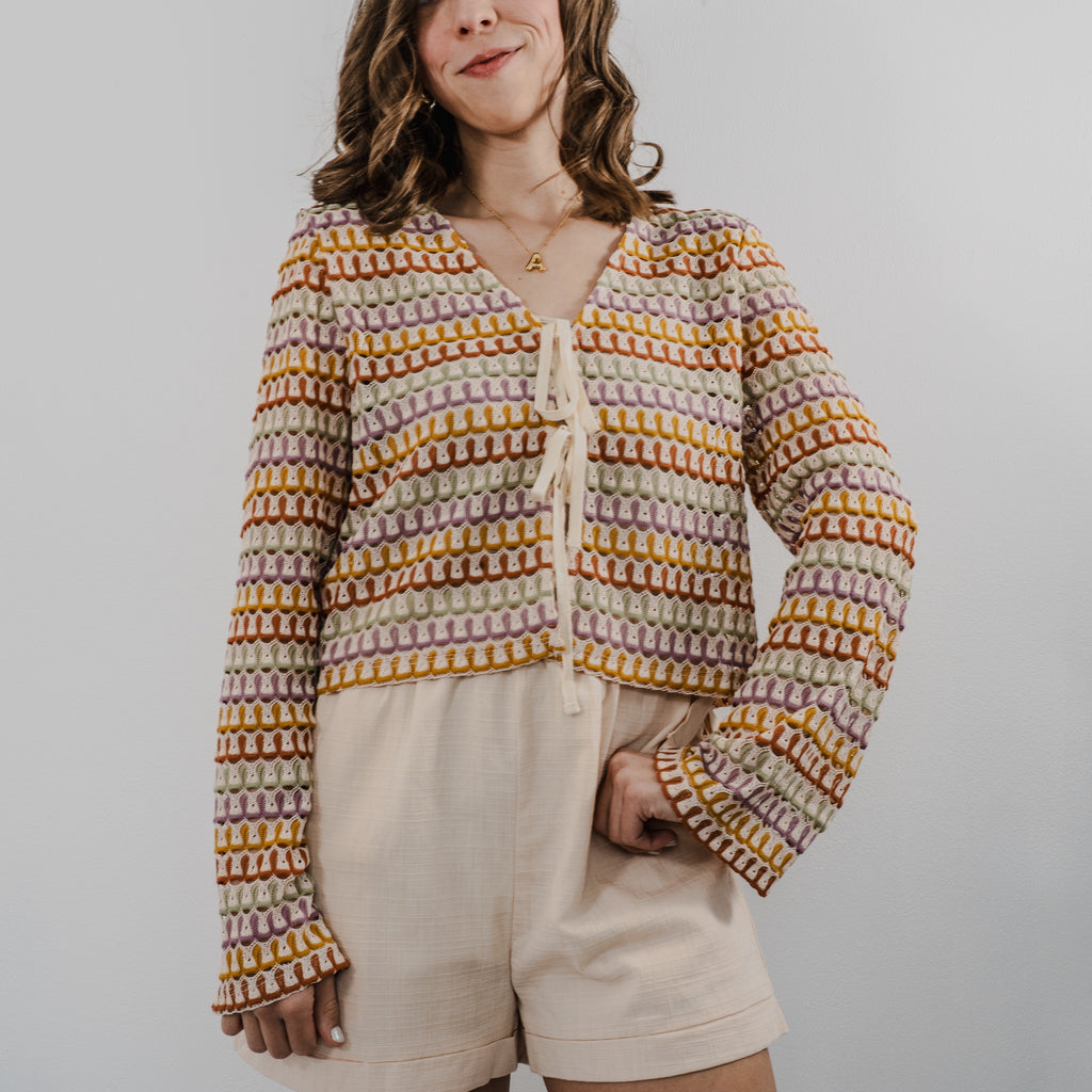 Model wearing a cream-colored, intricate heirloom crochet cardigan with long bell sleeves and a relaxed fit.