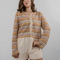 Model wearing a cream-colored, intricate heirloom crochet cardigan with long bell sleeves and a relaxed fit.