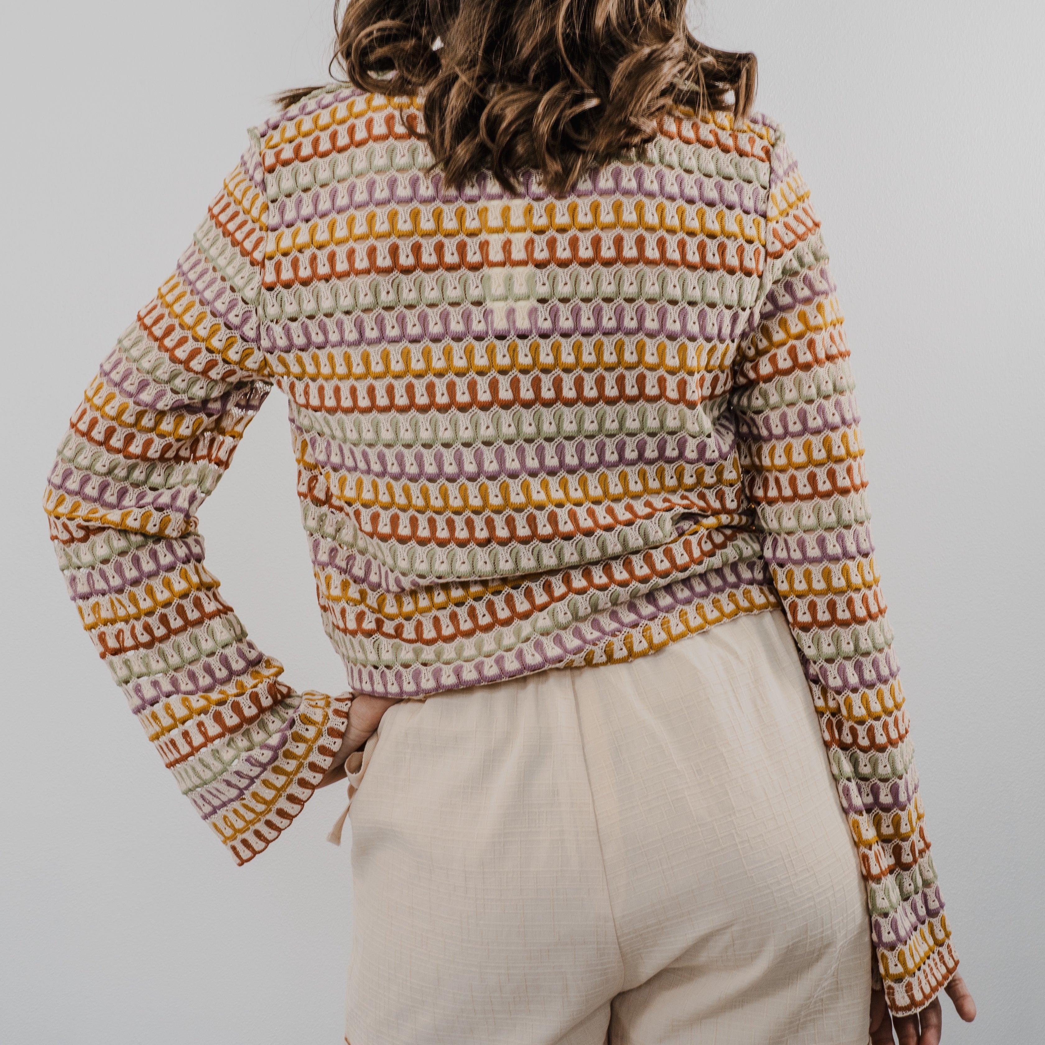 Back view of model wearing a cream-colored, intricate heirloom crochet cardigan with long sleeves and a relaxed fit.