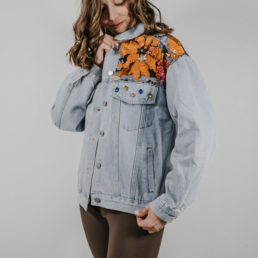 Model is holding the top and bottom of the jacket to show the sparkling sequins and mesh embroidery details on the Set Free denim jacket.
