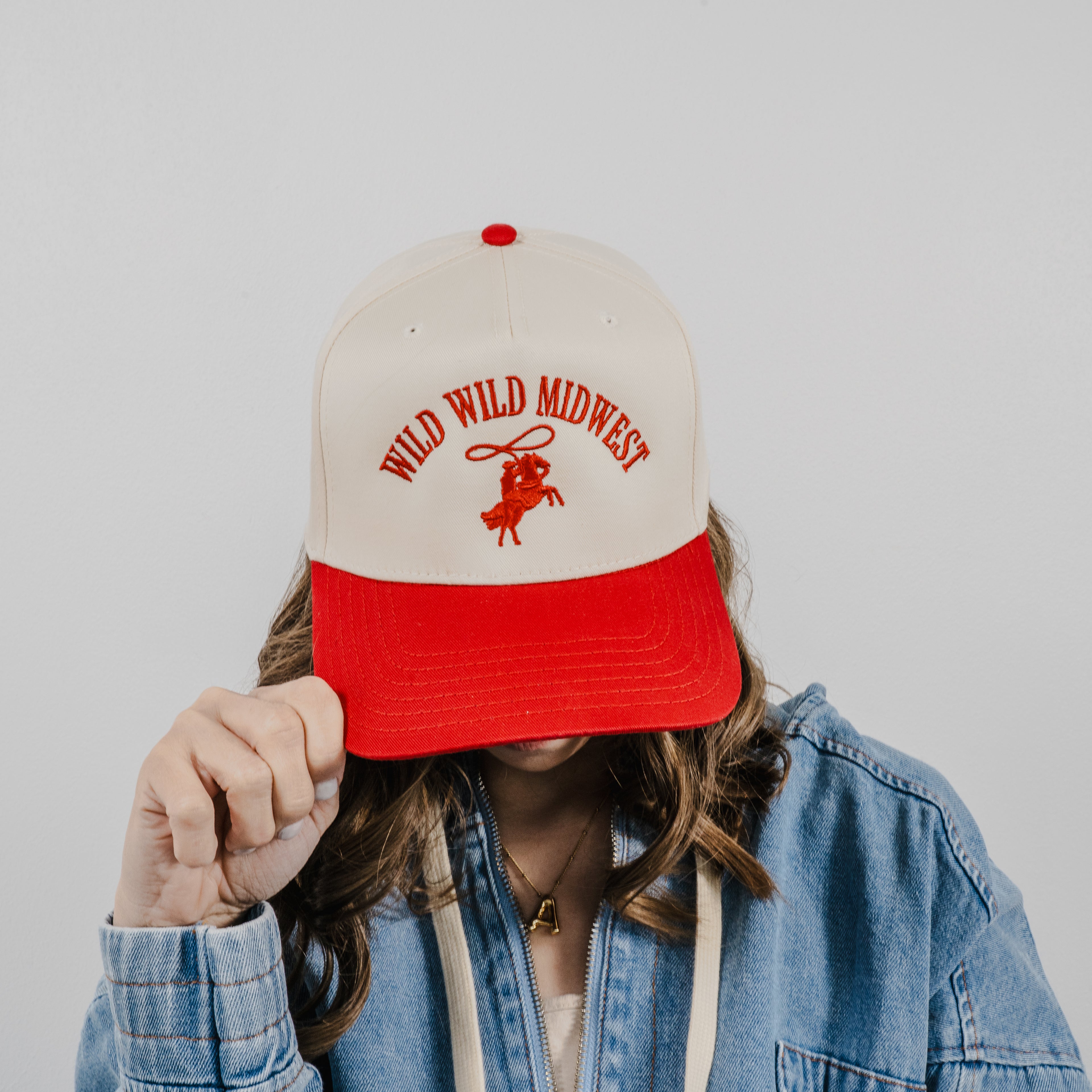Model wearing a close up of the Wild Wild Midwest Hat in beige and red with multi-colored western style embroidery.
