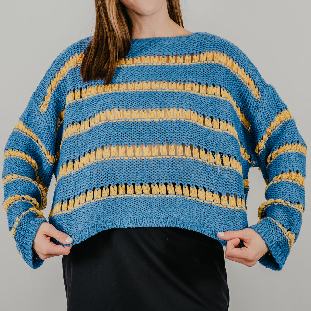 Model pulling sweater to show the full design on the oversized boxy fit of the "Ode to Gloria Knit Sweater"
