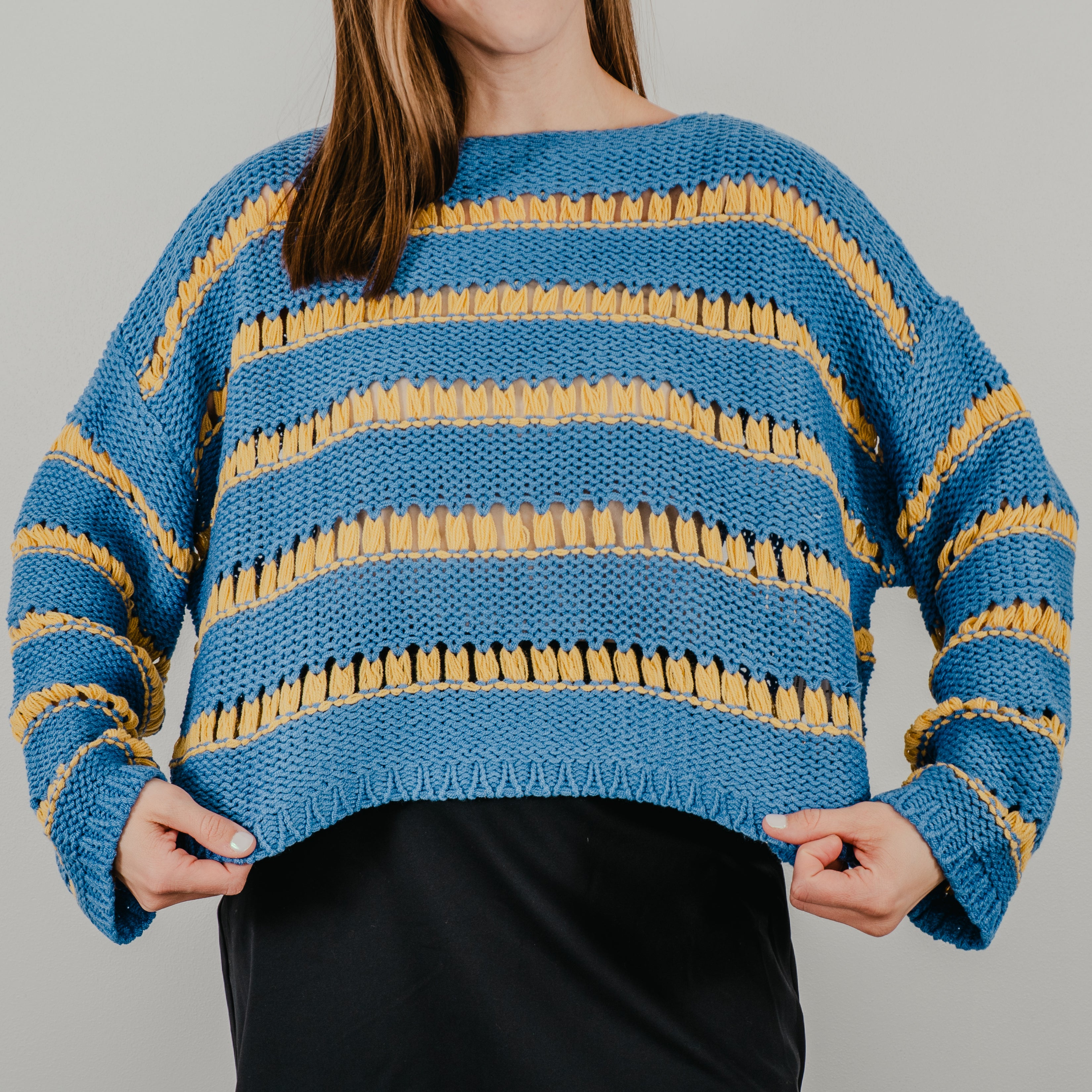 Model pulling sweater to show the full design on the oversized boxy fit of the "Ode to Gloria Knit Sweater"