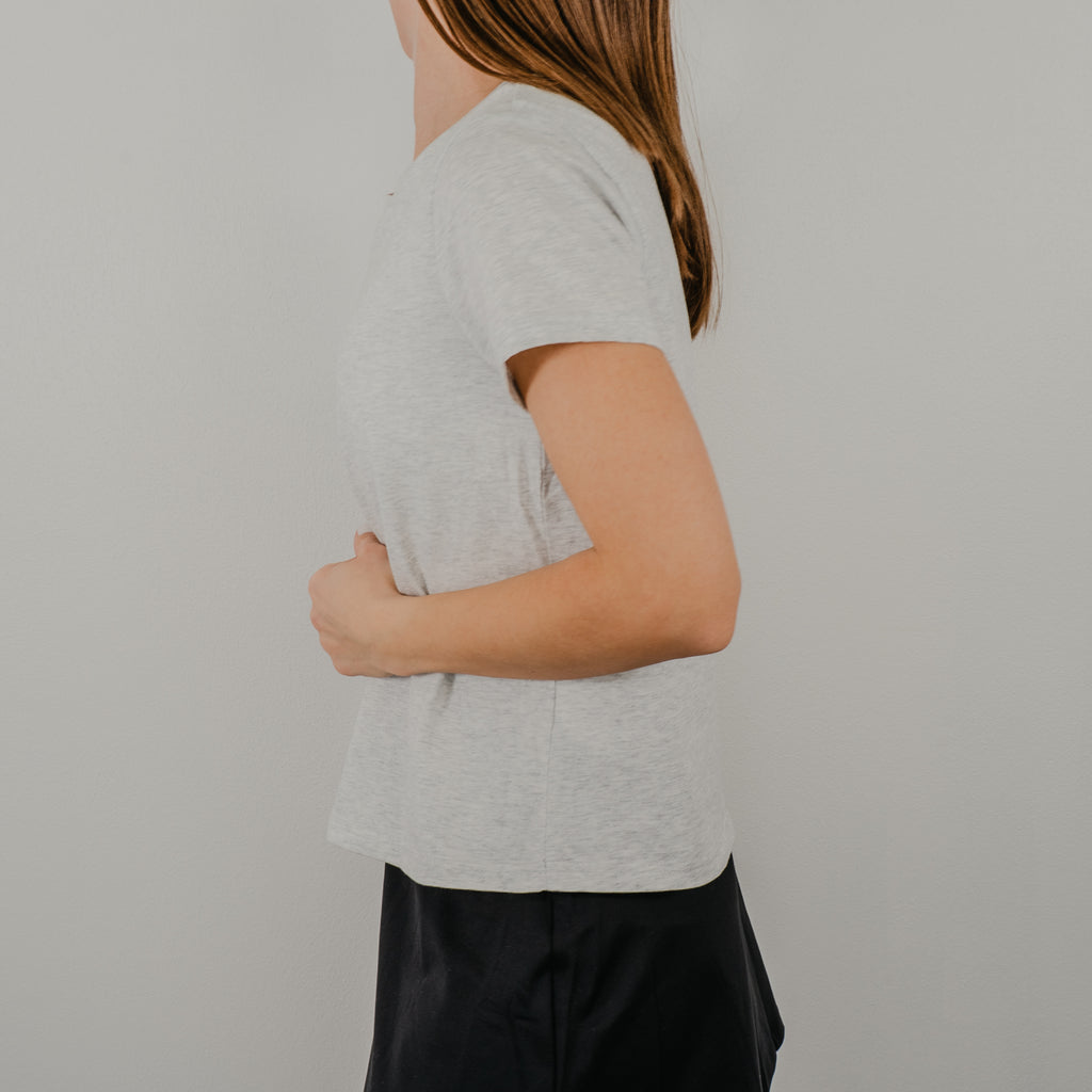 Side view of the light heathered grey Basic Bra Tee showing the clean, seamless design and where the shirt comes down to the waist in length.