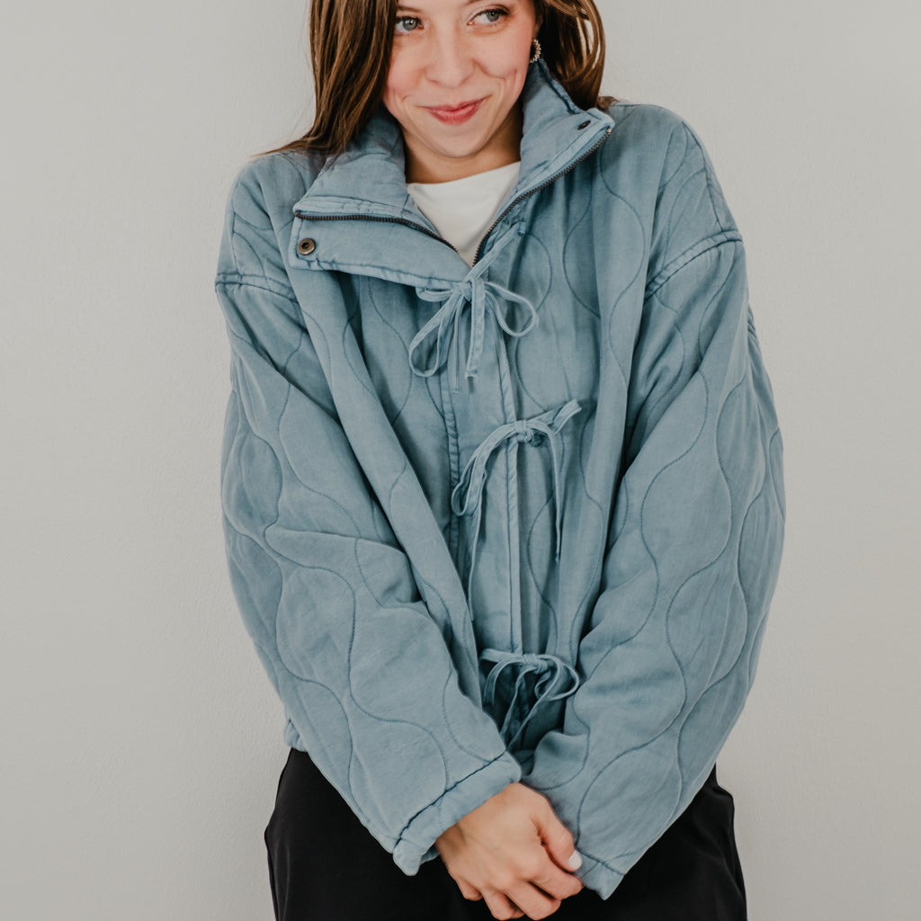 A view of the lightweight quilted jacket in dusty blue, featuring up close details of the curved quilting.
