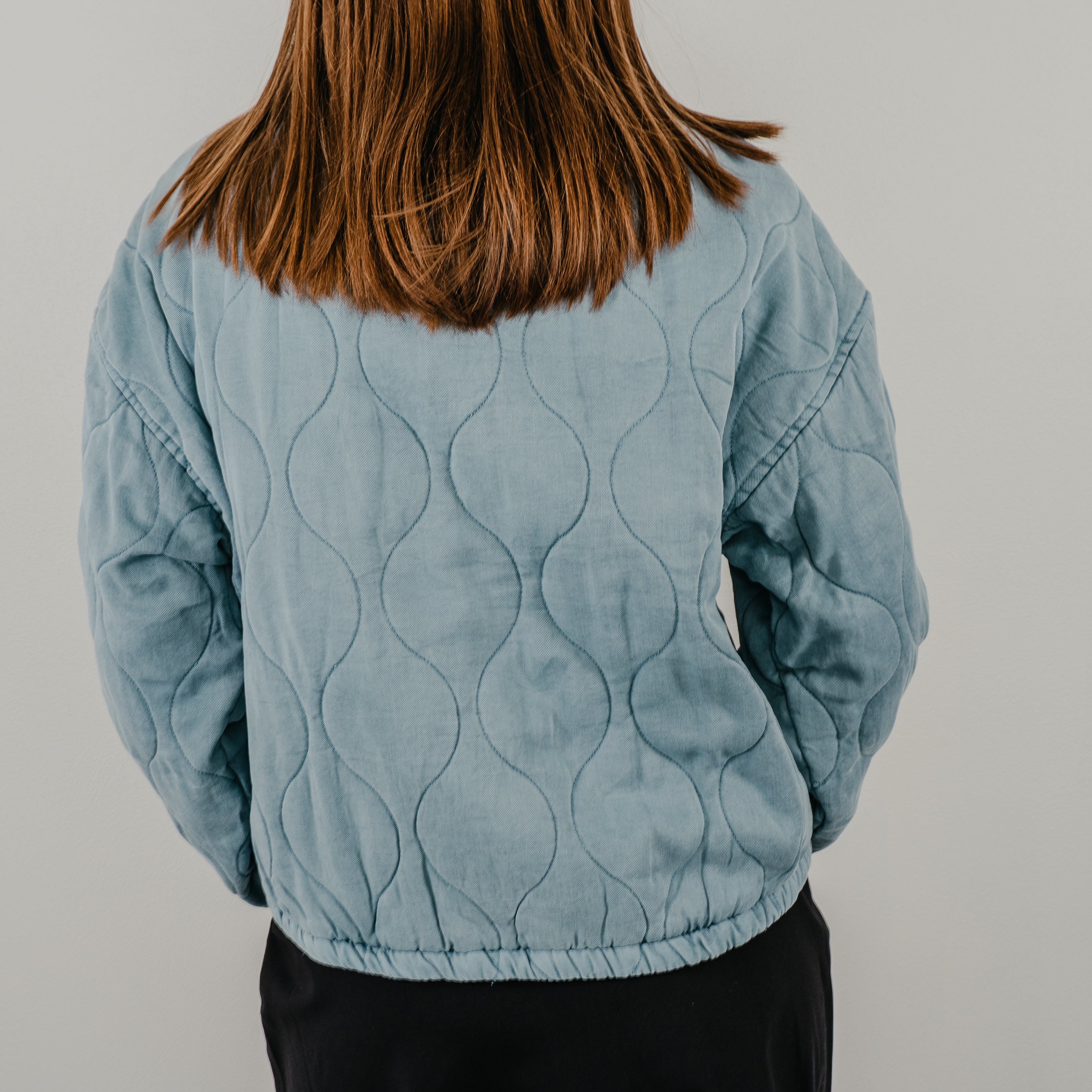 A back view of the Bow Front Quilted Jacket in dust blue showing the curved detailing.
