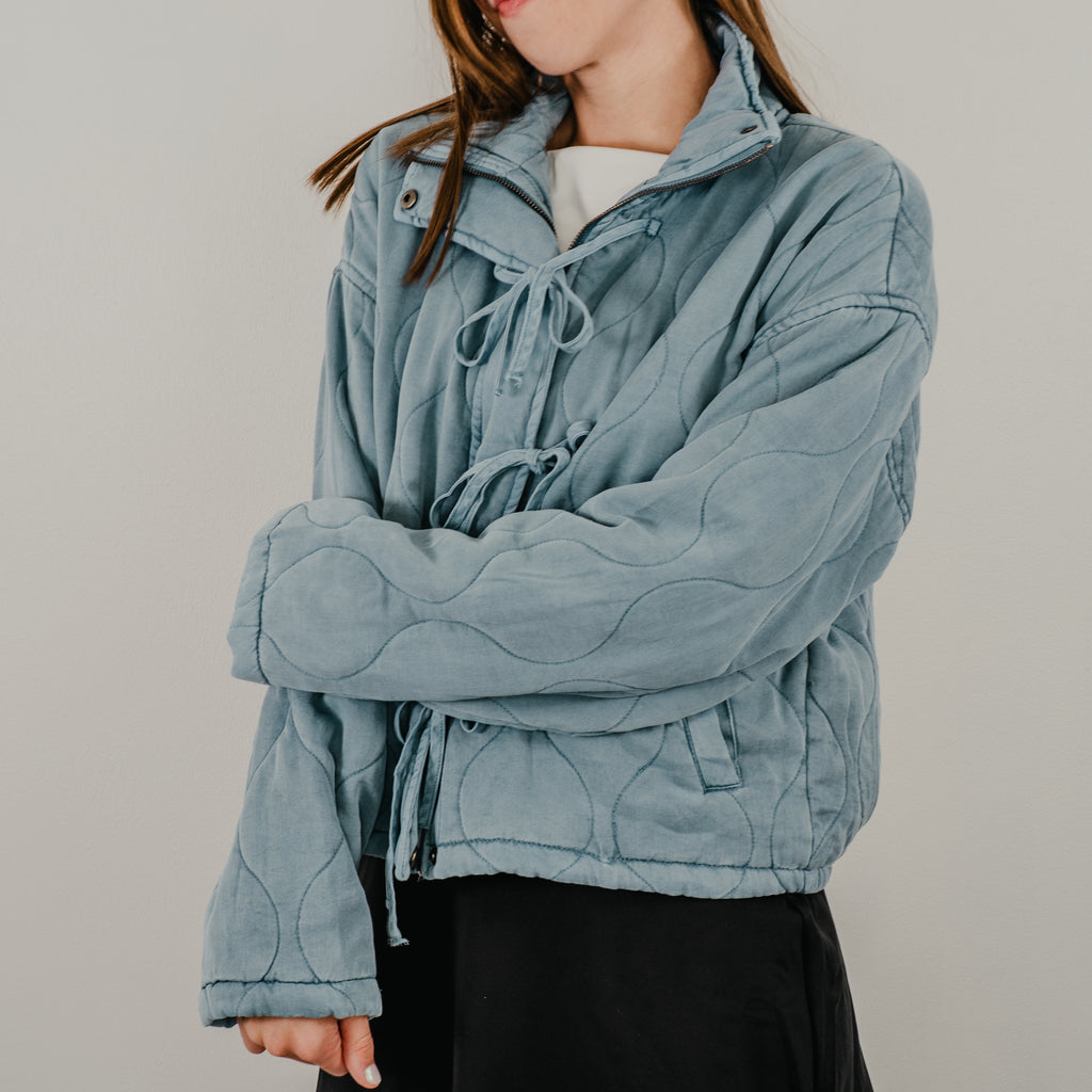 A view of the lightweight quilted jacket in dusty blue, featuring up close details of the curved quilting.