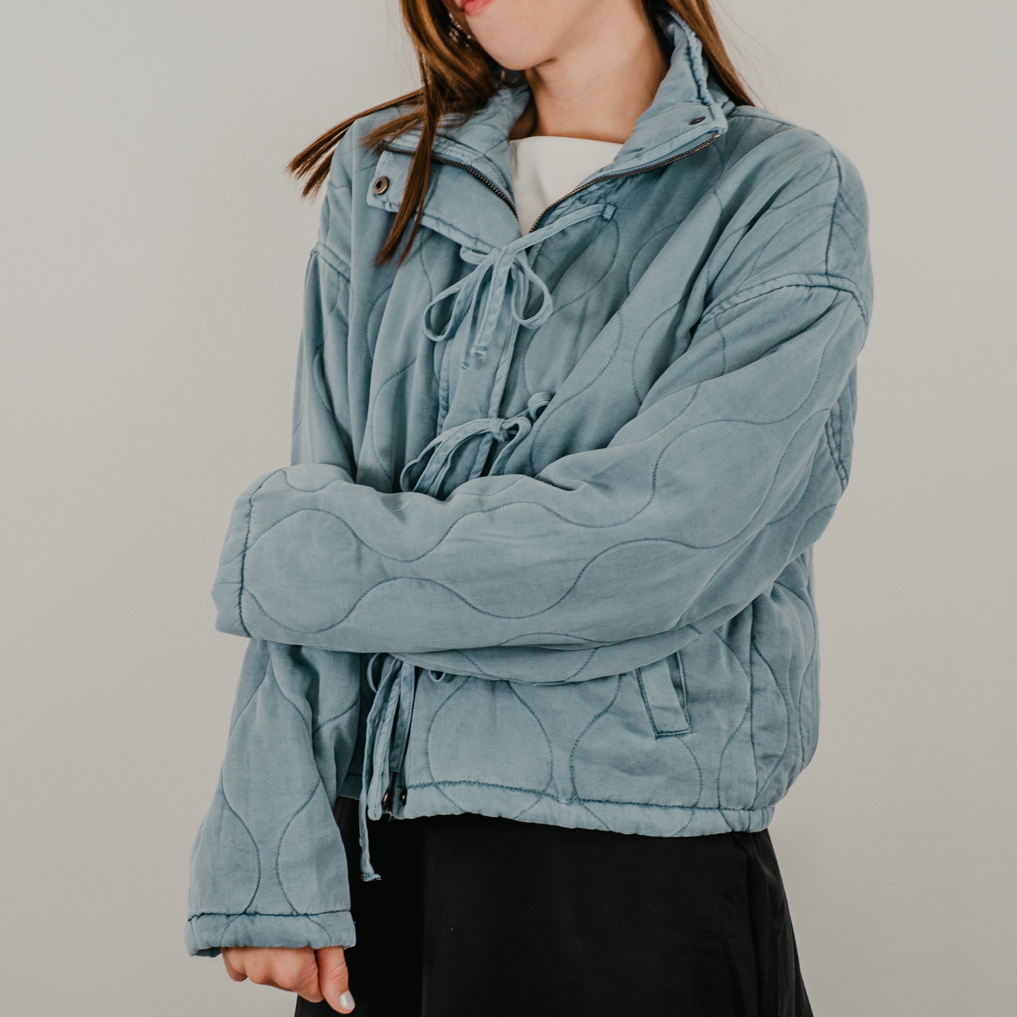 A view of the lightweight quilted jacket in dusty blue, featuring up close details of the curved quilting.