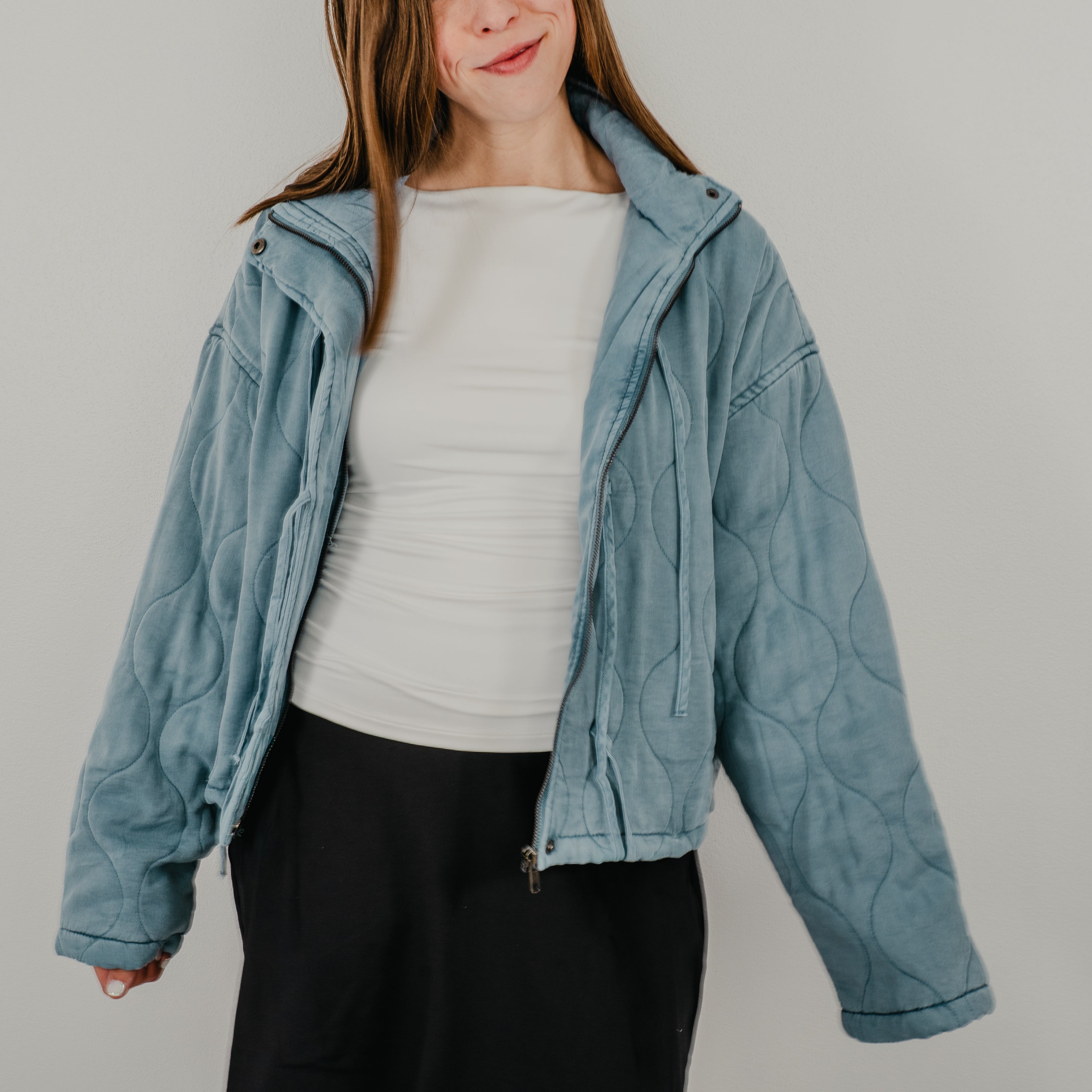 An unzipped view of the lightweight quilted jacket in dusty blue, featuring dangling tie closures down the front and showing optional snap buttons.
