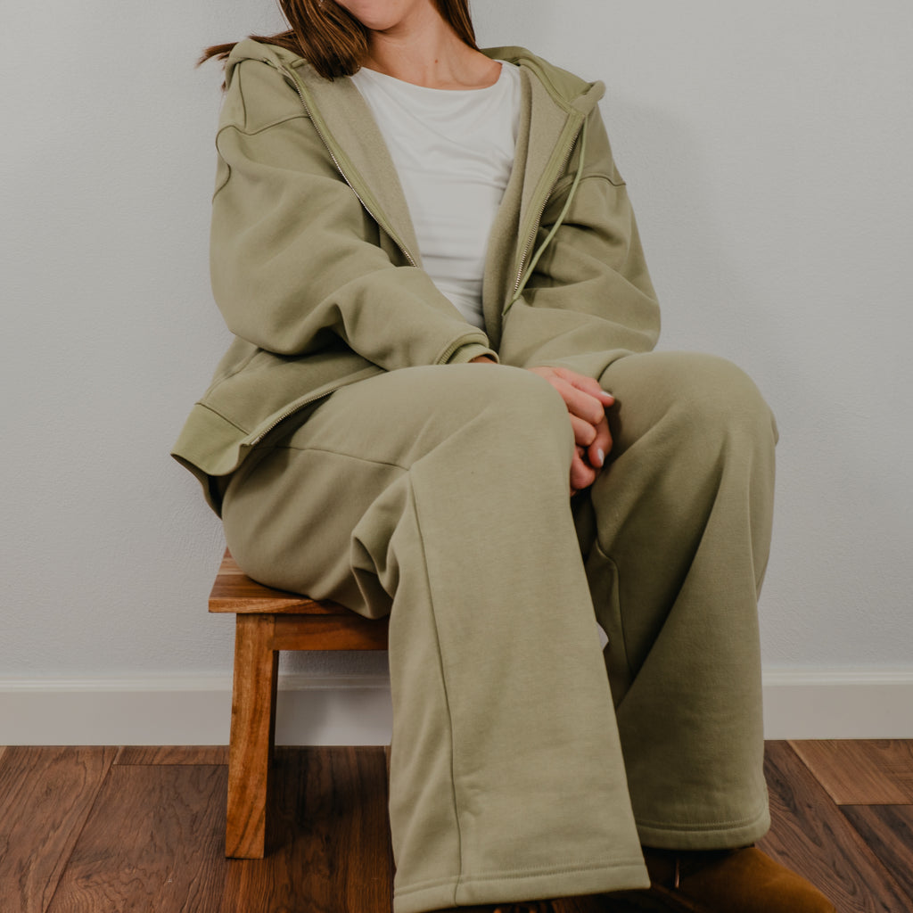 Shows model wearing a two-piece lounge set in a deep fern green, featuring a matching oversized full zip sweatshirt and relaxed-fit joggers.