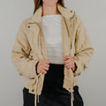 An unzipped view of the lightweight quilted jacket in oatmeal, a light tan, featuring dangling tie closures down the front and showing optional snap buttons.