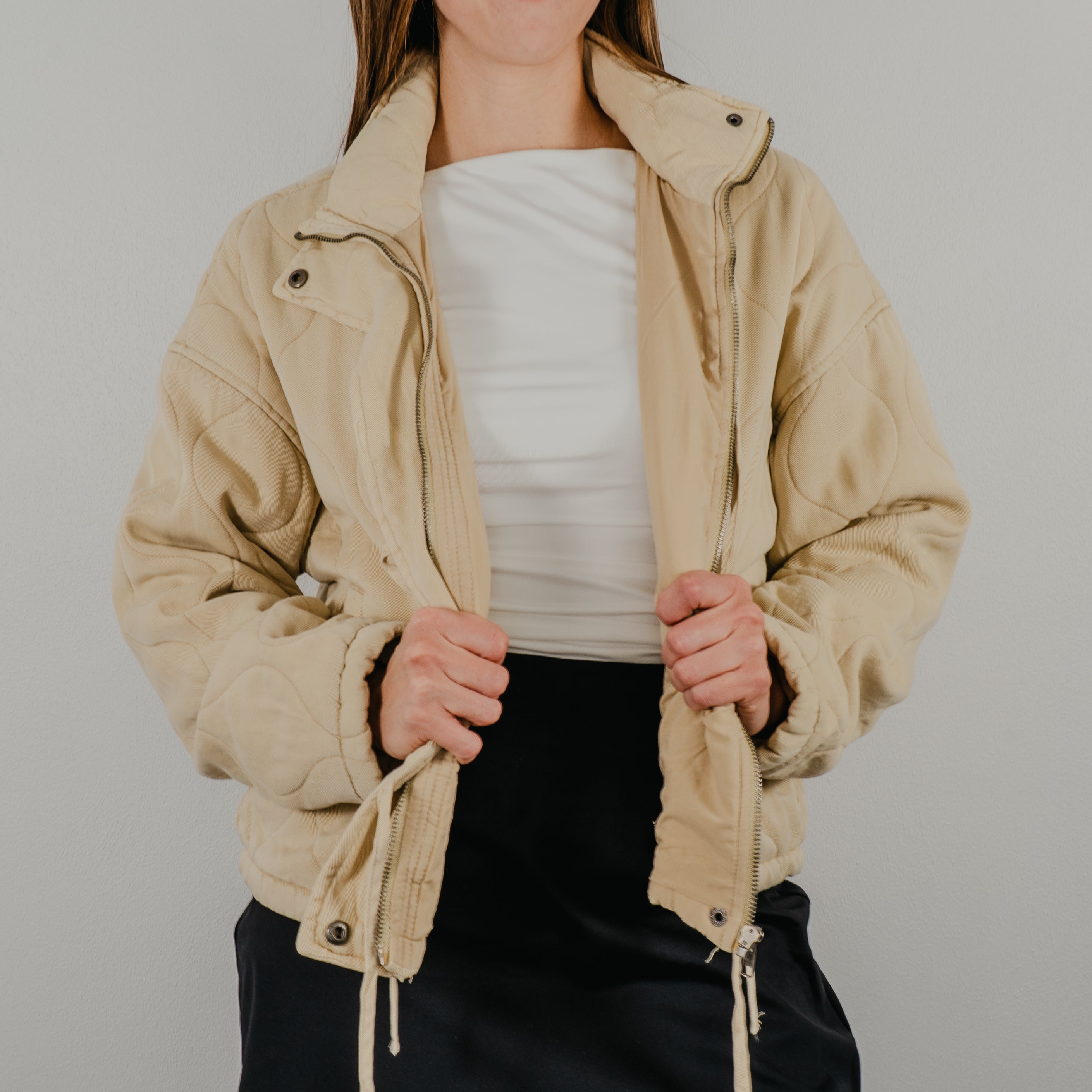 An unzipped view of the lightweight quilted jacket in oatmeal, a light tan, featuring dangling tie closures down the front and showing optional snap buttons.