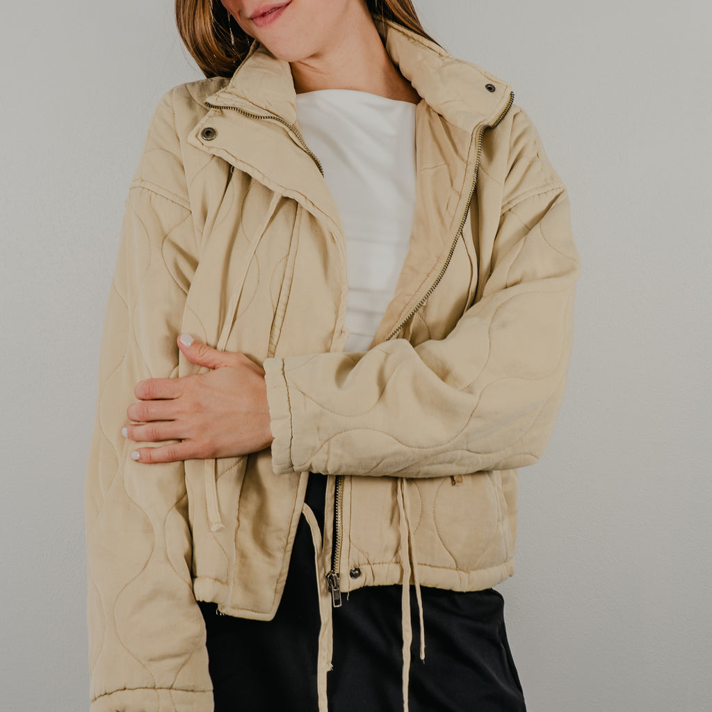 An unzipped view of the lightweight quilted jacket in oatmeal, a light tan, featuring dangling tie closures down the front and showing optional snap buttons.