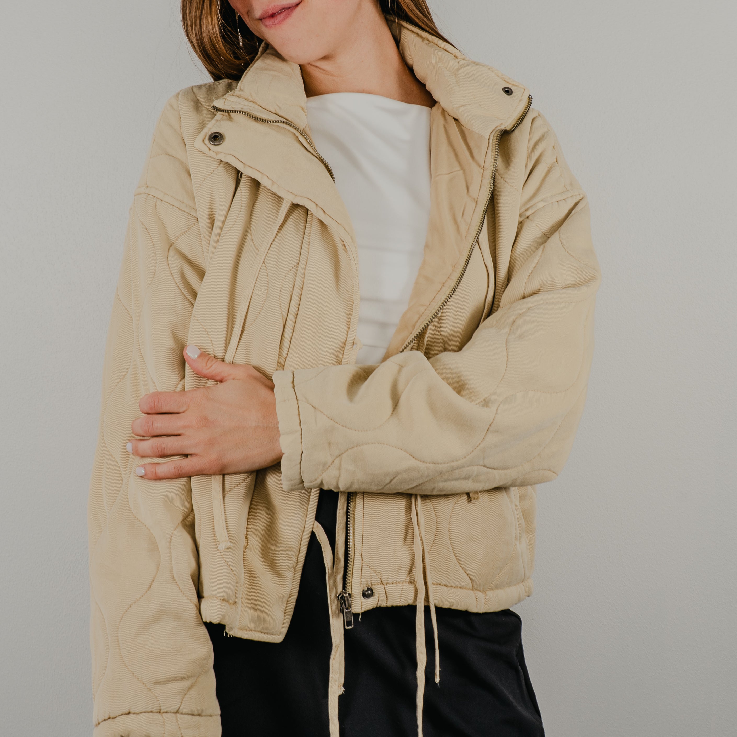 An unzipped view of the lightweight quilted jacket in oatmeal, a light tan, featuring dangling tie closures down the front and showing optional snap buttons.