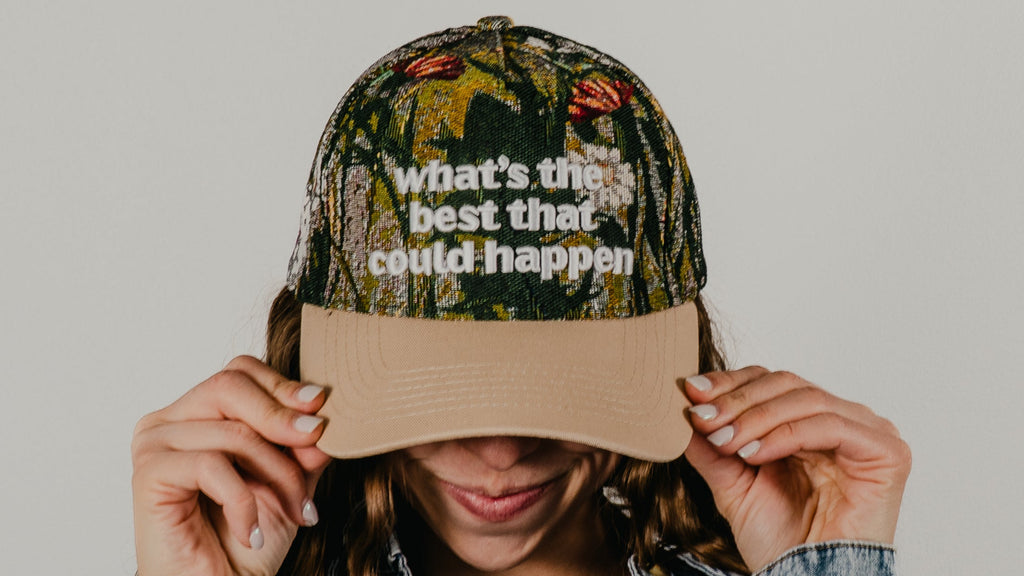 Person wearing a camouflage cap with text and a denim jacket on a plain background