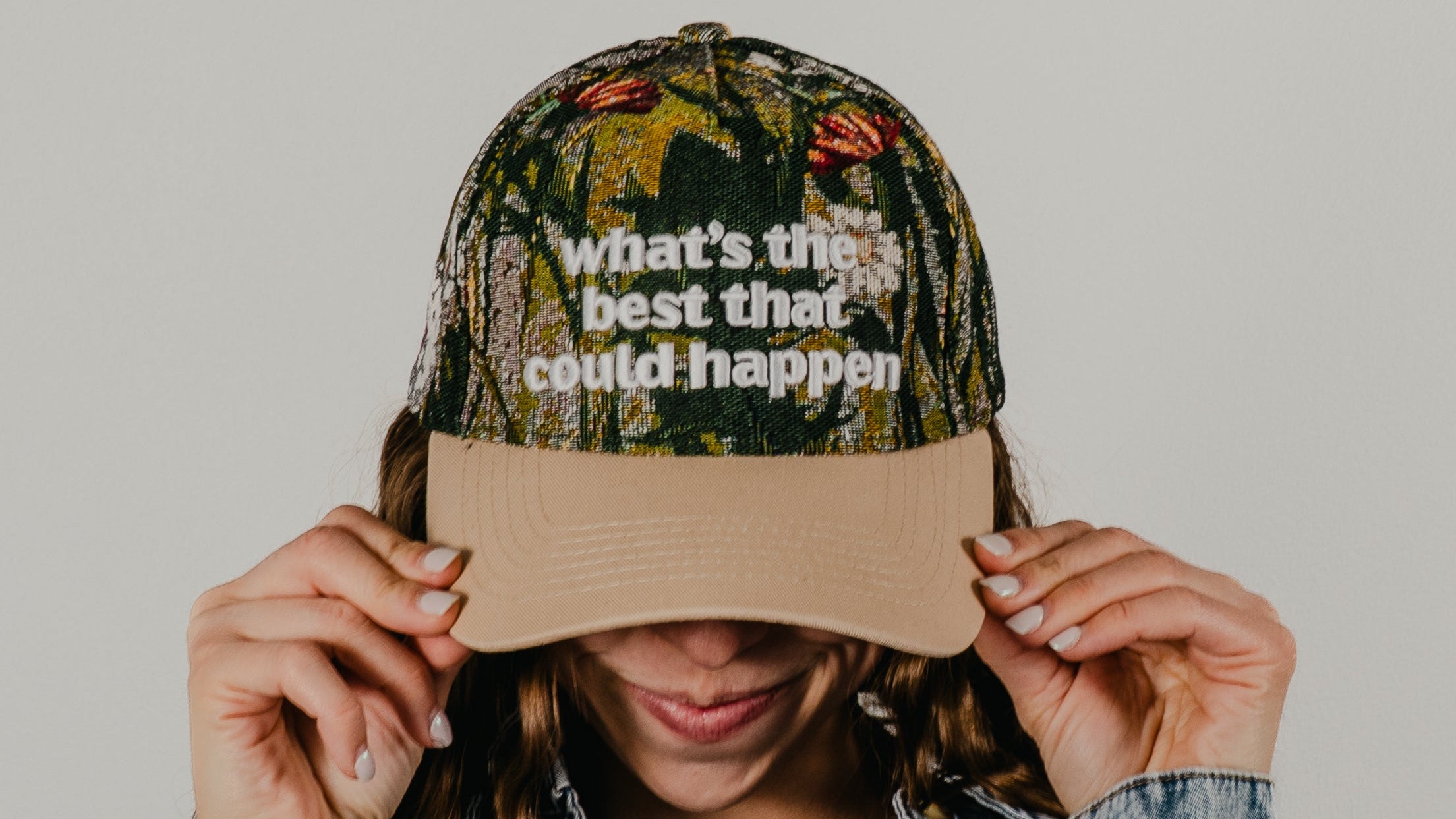 Person wearing a camouflage cap with text and a denim jacket on a plain background