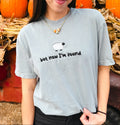 A woman wearing a light blue-gray graphic t-shirt with a cartoon sheep and the text 'but now I'm found' in front of a fall harvest background with pumpkins and dried leaves.