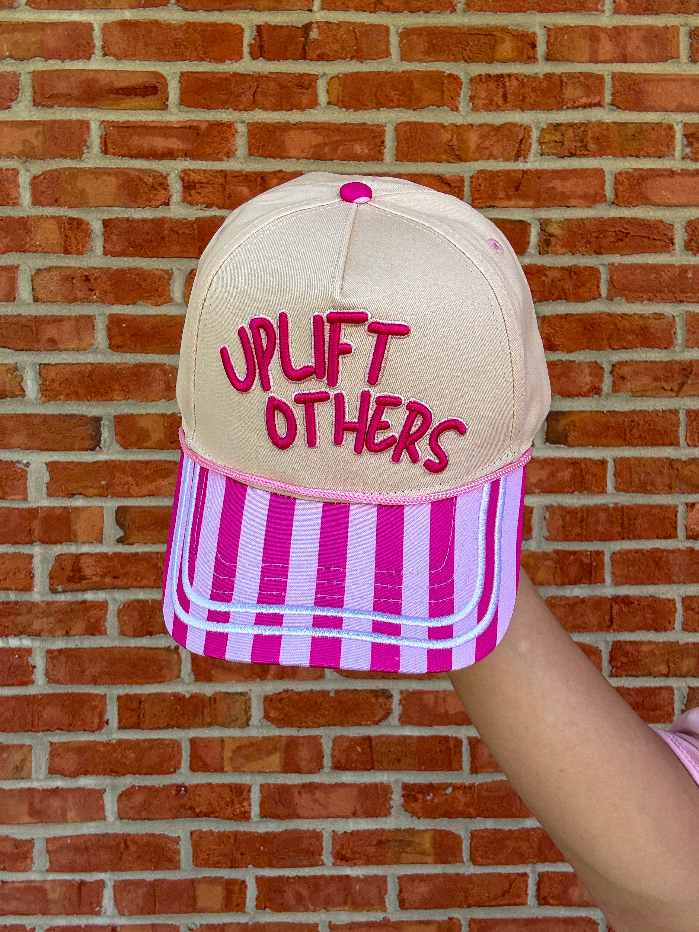 Uplift others ball cap against brick wall held up by an arm