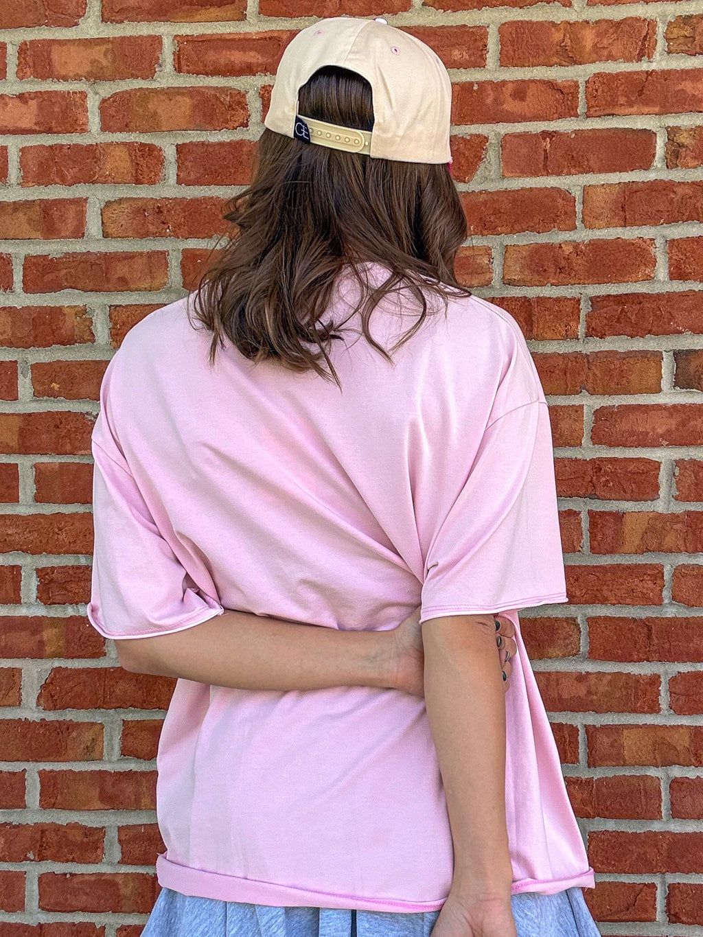 Person wearing a pink oversized shirt and blue skirt against a brick wall