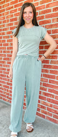 Woman wearing a light blue jumpsuit standing against a brick wall.