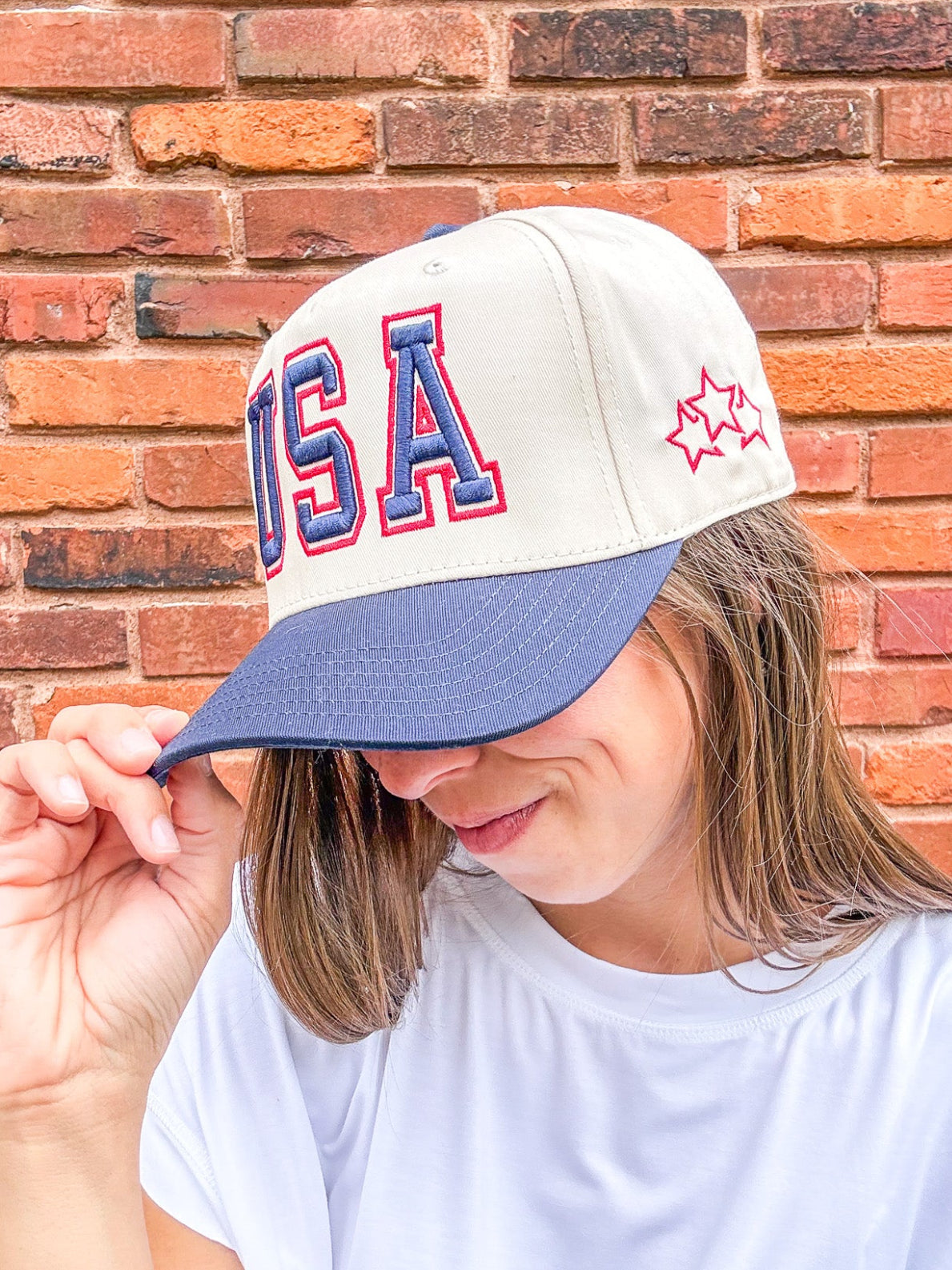 Person wearing a cap with 'USA' and a star design against a brick wall.