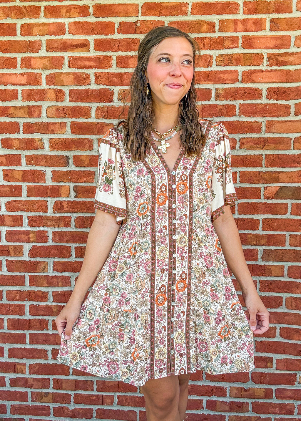 Woman wearing a floral dress standing against a brick wall