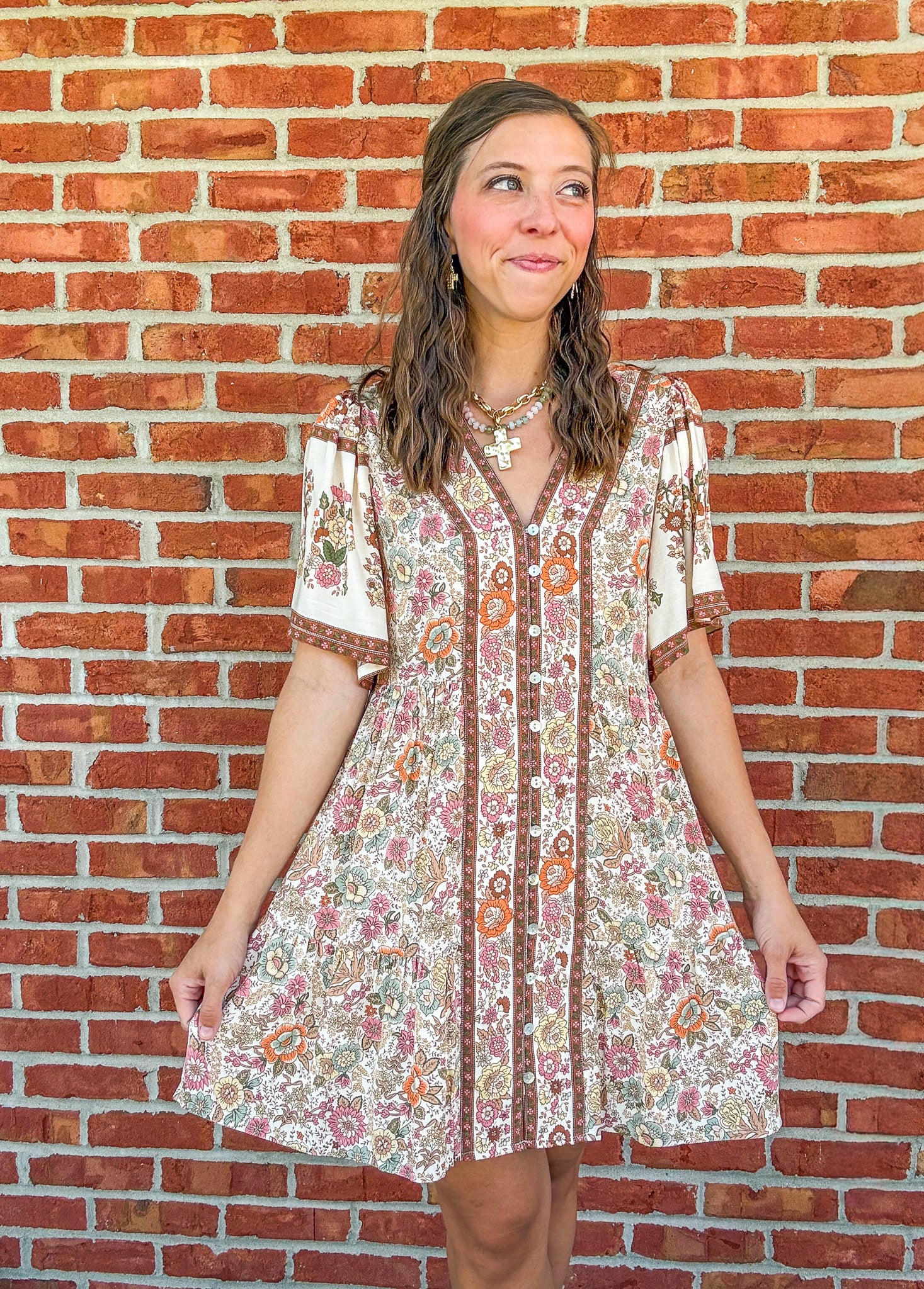 Woman wearing a floral dress standing against a brick wall