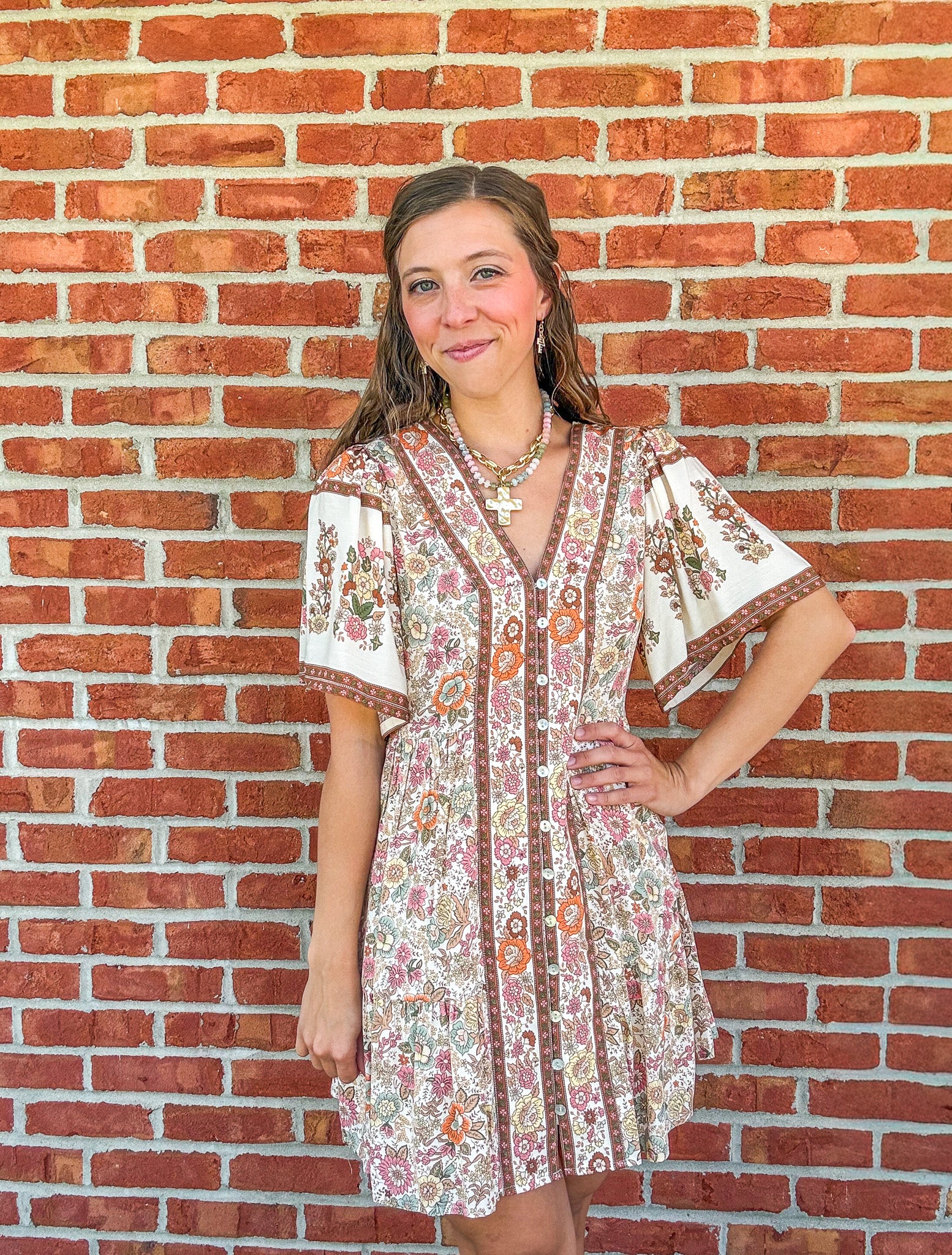 Woman wearing a floral dress standing against a brick wall