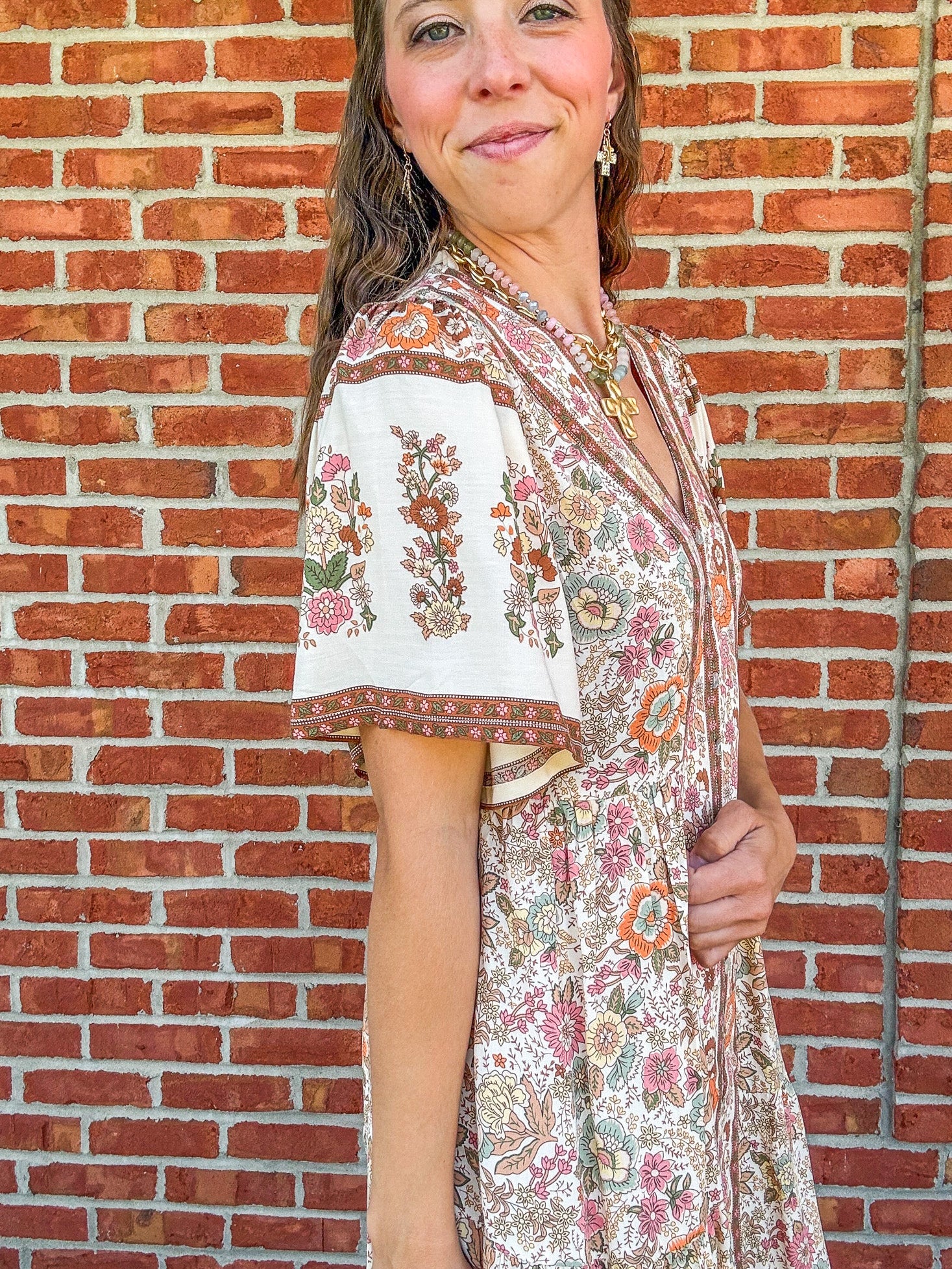 Woman wearing a floral dress standing in front of a brick wall