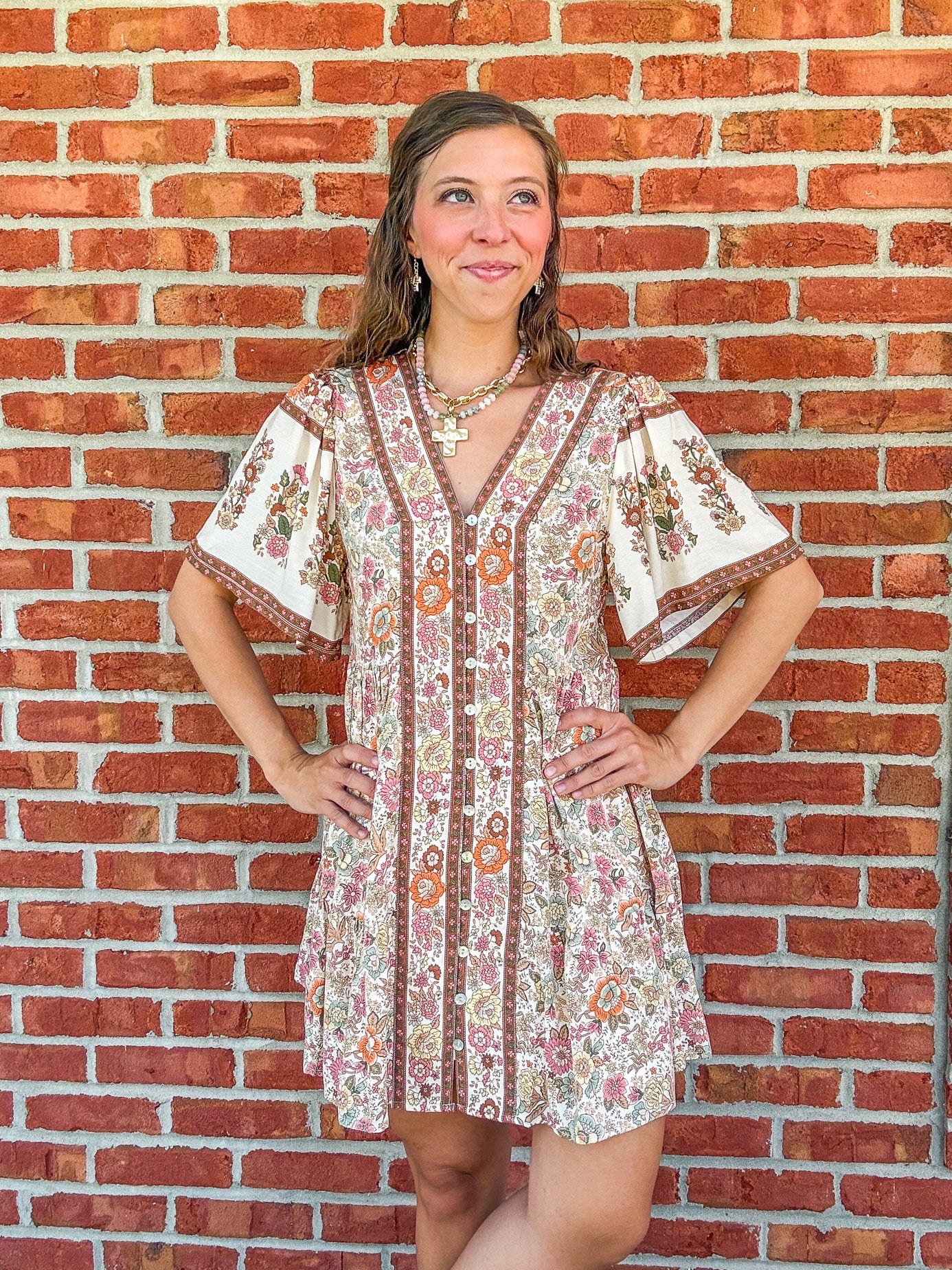 Woman wearing a floral dress standing against a brick wall