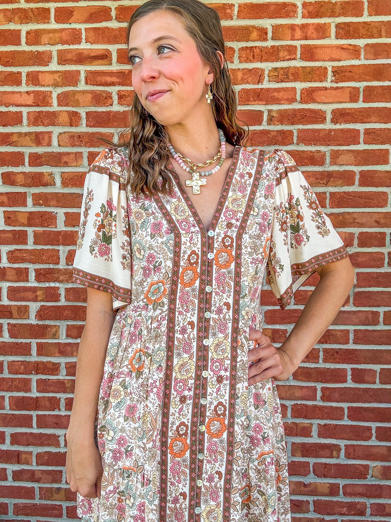 Woman wearing a floral dress standing against a brick wall