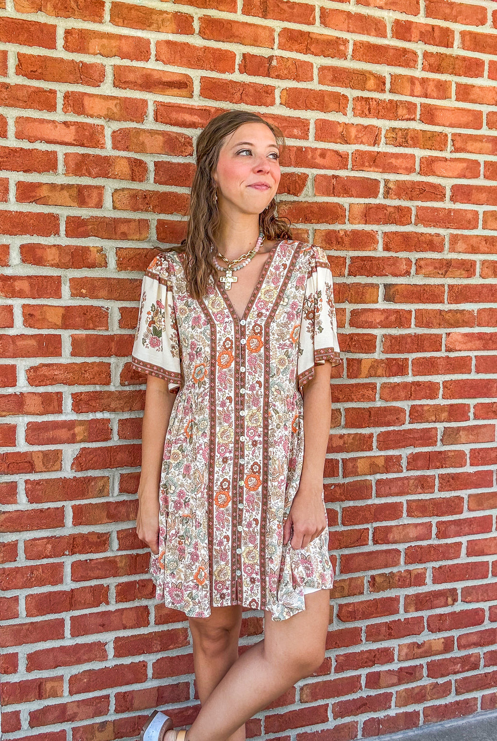 Woman wearing a patterned dress standing against a brick wall