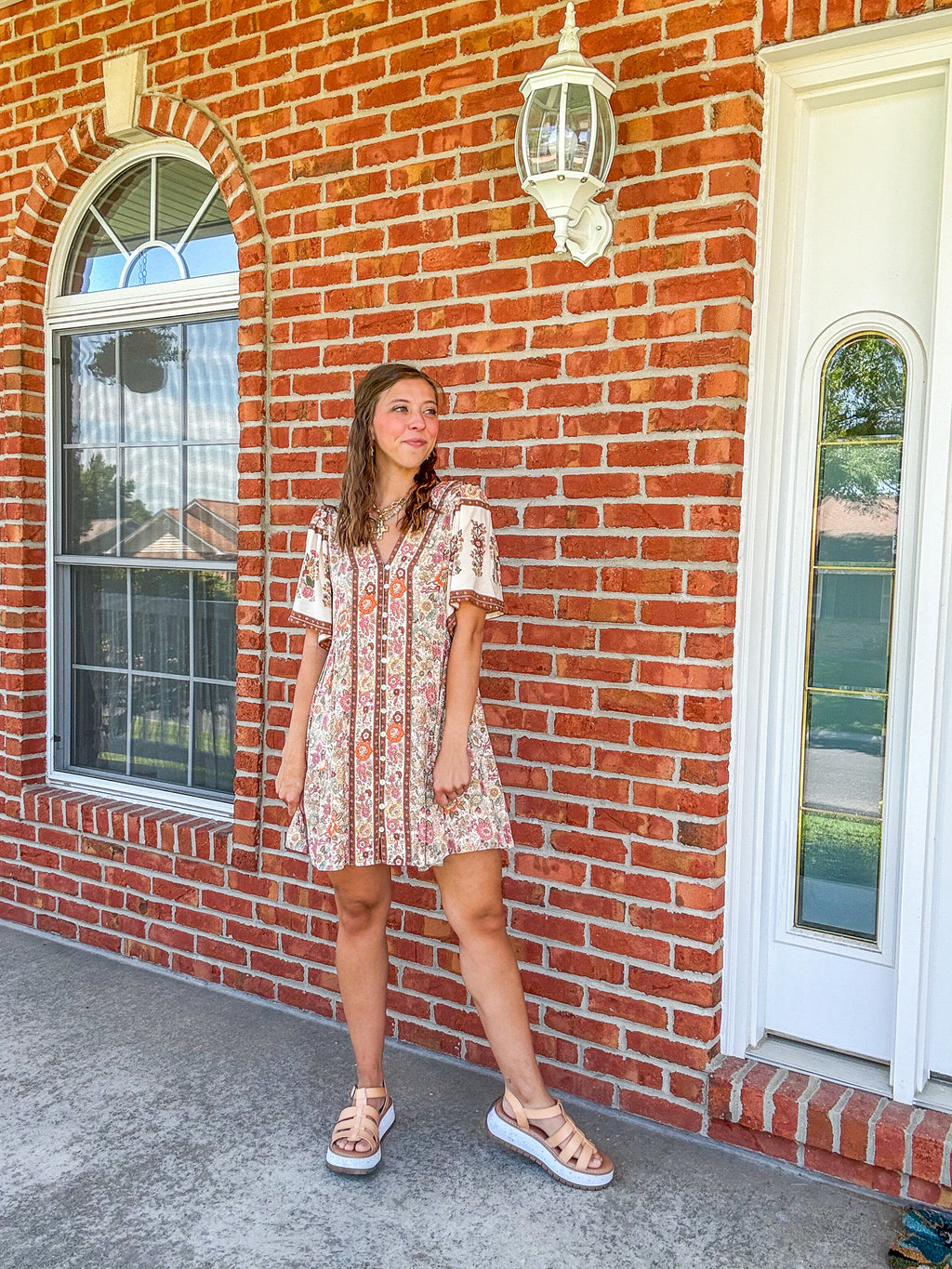 Woman in a floral dress standing in front of a brick building