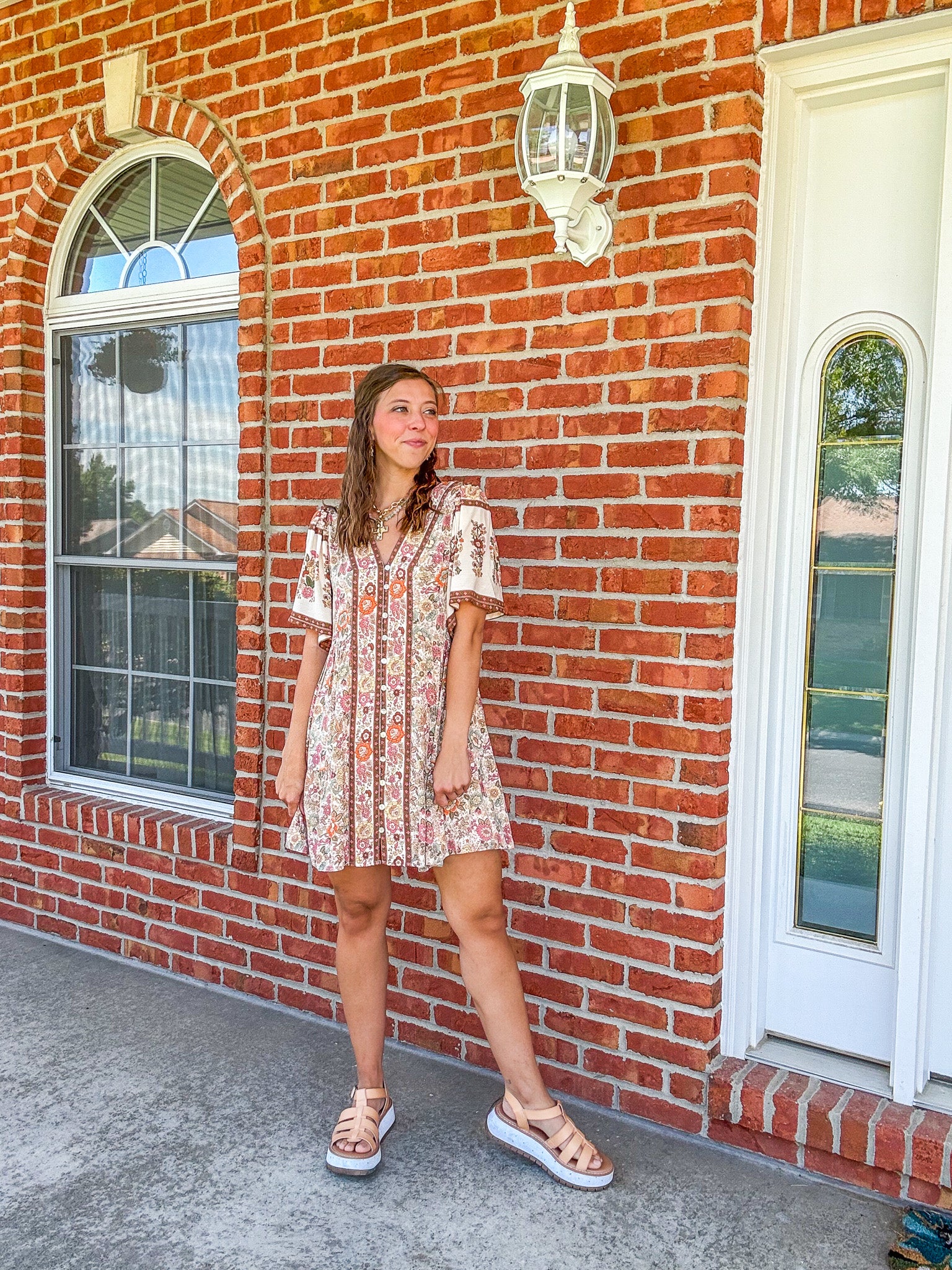 Woman in a floral dress standing in front of a brick building