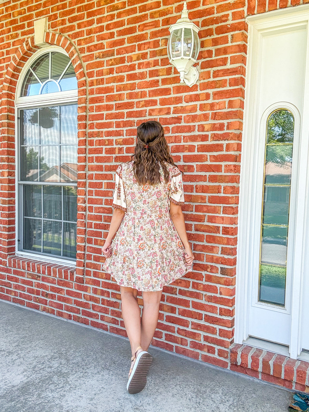 Woman in a floral dress standing in front of a brick building with white windows.