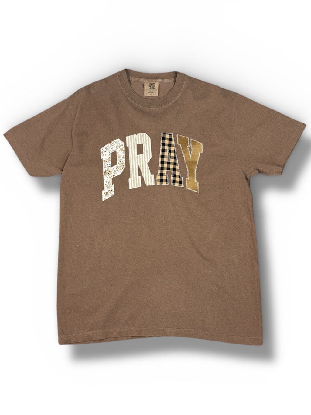 "Classic brown crewneck t-shirt with 'Pray' delicately embroidered in a minimalist script on the chest. Letters each have a different pattern.
