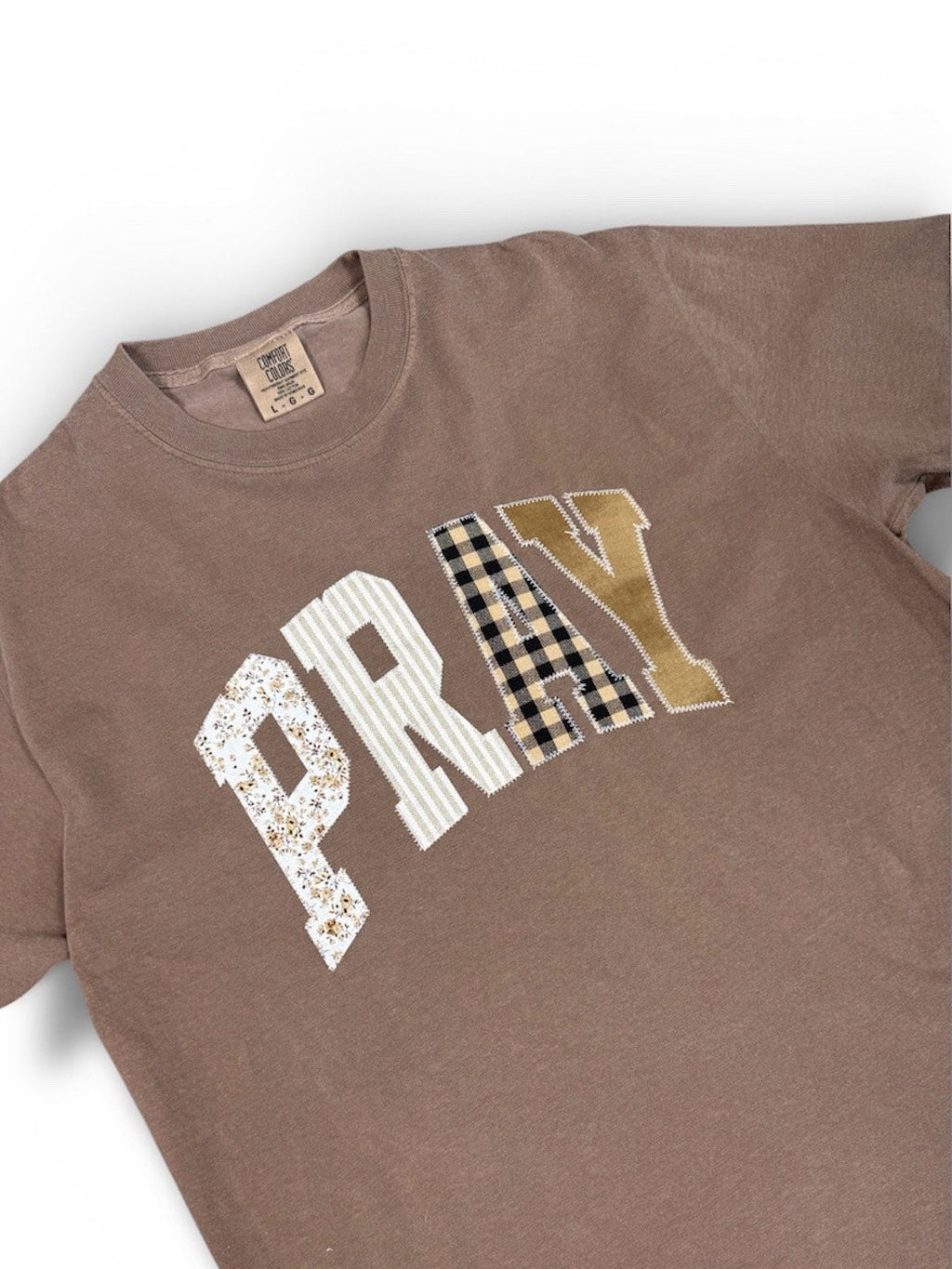 Close-up of the fine-thread embroidery detail on the Pray Embroidered Tee. Floral, stripe, plaid, and solid fabric design.
